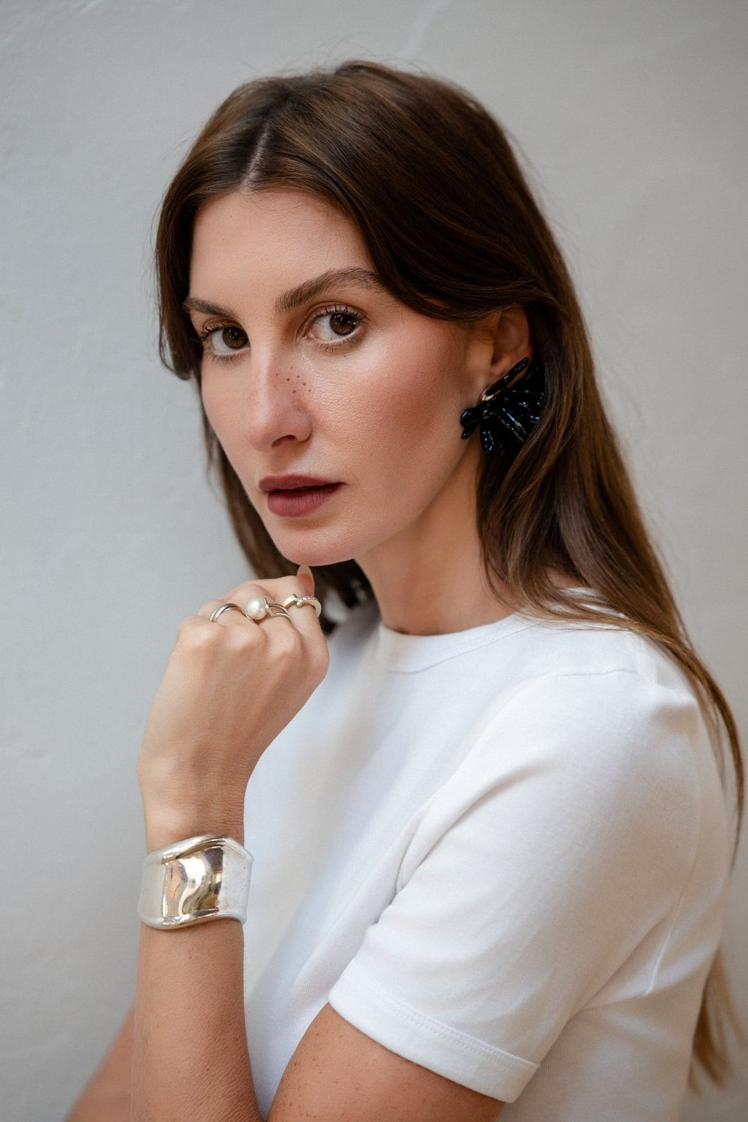 Allison Bornstein headshot in a white tee, hand at her collarbone, silver cuff and sculptural black earring.
